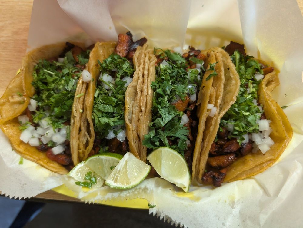 Al pastor street tacos topped with cilantro and onion, served with lime wedges